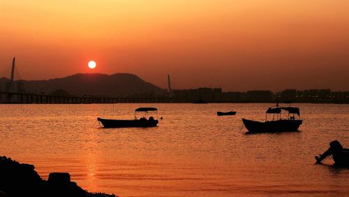 Silhouette boats in sea against orange sky