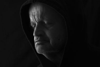 Close-up of man wearing hood against black background