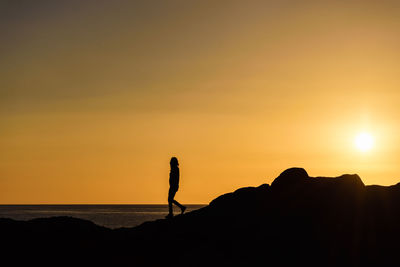 Silhouette person walking on cliff against orange sky
