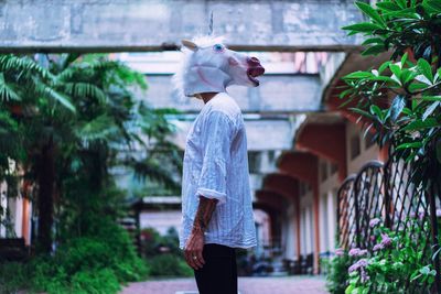 Side view of man wearing mask while standing against building