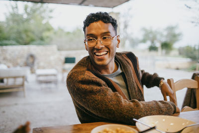 Happy young man wearing eyeglasses sitting at dining table in patio