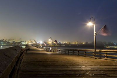 Illuminated pier by sea against sky at night