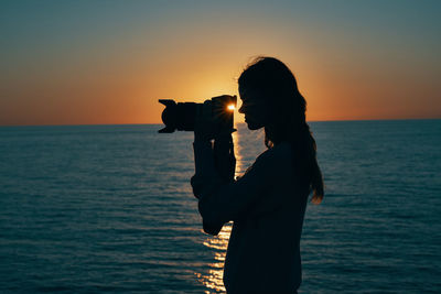 Silhouette woman standing by sea against sky during sunset