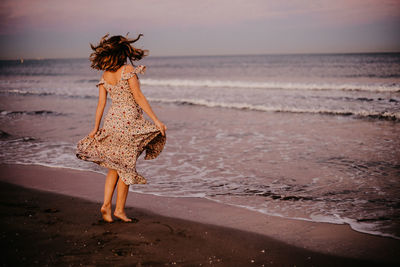 Woman walking on beach against sea during sunset