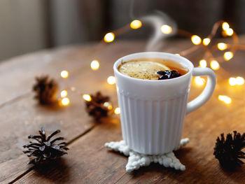 White cup of hot tea with lemon. pine cones and light bulbs on shabby wooden background.