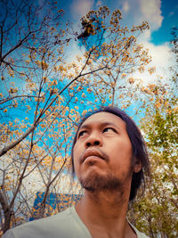 Young man looking away against trees