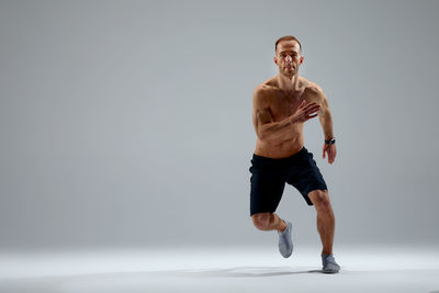 Full length of shirtless man exercising against white background