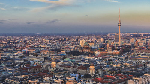 Fernsehturm amidst cityscape against sky during sunset