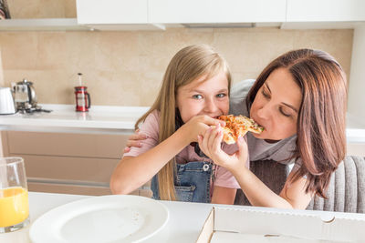 Portrait of mother and daughter eating food at home