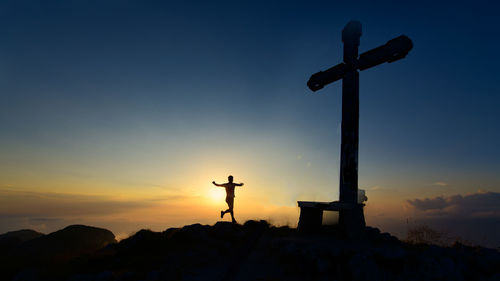 Mountain runner comes to the top where there is a cross at sunset