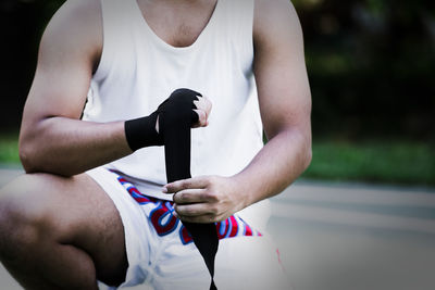 Midsection of boxer tying bandage while crouching on road