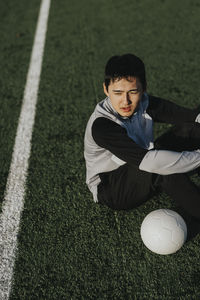 High angle view of male athlete with soccer ball while sitting at sports field