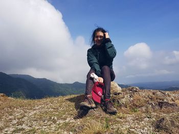 Full length portrait of young woman sitting on field against sky