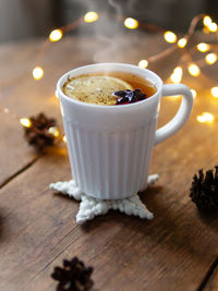 White cup of hot tea with lemon. pine cones and light bulbs on shabby wooden background.