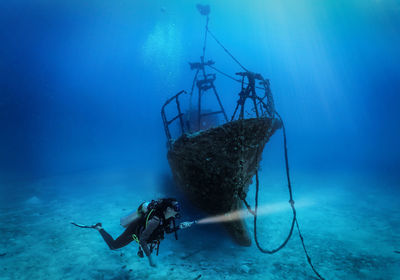 Scuba driver swimming by shipwreck undersea