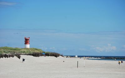 Lighthouse on beach against blue sky