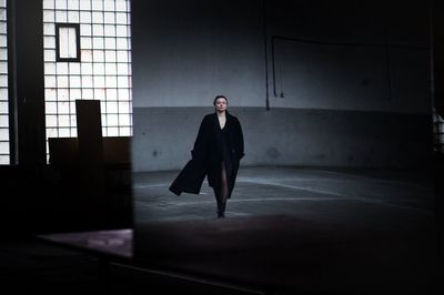 Full length portrait of young man standing against dark wall