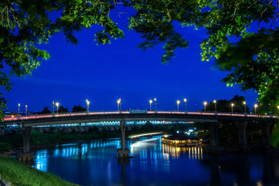 Illuminated bridge over river against blue sky at night