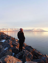 Man standing on rock by lake against sky