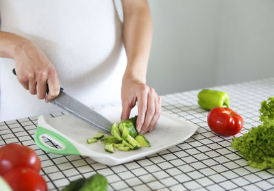 Midsection of woman chopping cucumber in plate