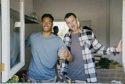 Portrait of smiling male friends standing in kitchen seen through window