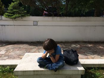 High angle view of sad boy sitting with backpack on retaining wall