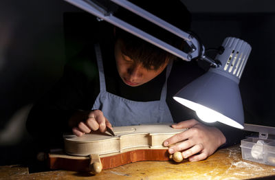 Male craftsman violin maker working on a new violin in the workshop