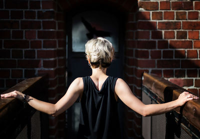 Rear view of woman standing against brick wall