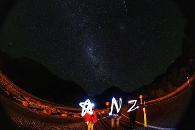 People holding illuminated alphabets against starry sky