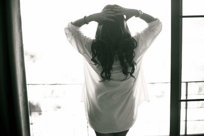 Rear view of woman with hands behind head standing on balcony