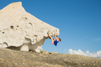Woman climbing rock against clear blue sky