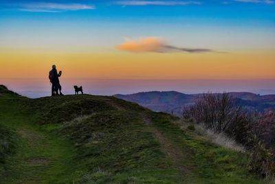 Hikers standing with dog on mountain against sky during sunset
