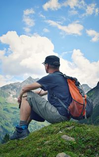 Side view of man sitting on field against mountain