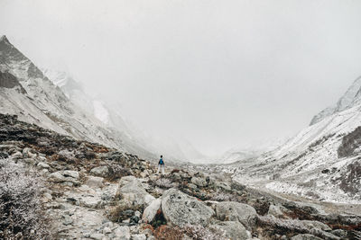 Scenic view of snowcapped mountains with person standing on rock against sky