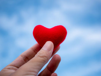 Close-up of hand holding heart shape against sky