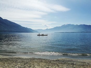 Distant view of diving platform in sea by mountains against sky