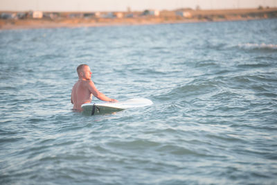Rear view of shirtless male surfer with surfboard in sea