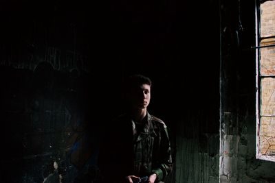 Young man looking away while standing in abandoned building