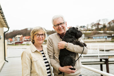 Portrait of smiling senior couple with schnauzer at beach against sky