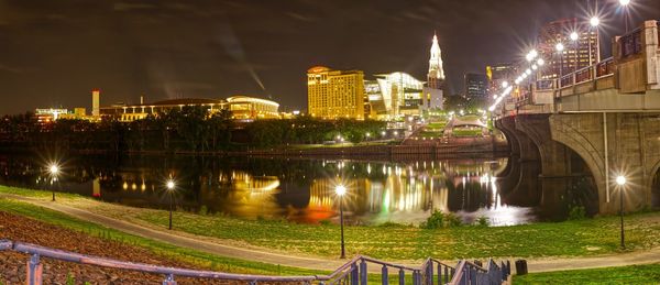 Illuminated bridge over river by buildings in city at night