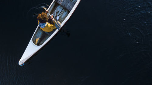 Young man paddling through oar while sitting in canoe on river