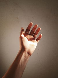 Sunlight falling on cropped hand of person against wall