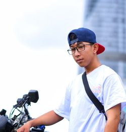 Portrait of young man with bicycle standing against clear sky