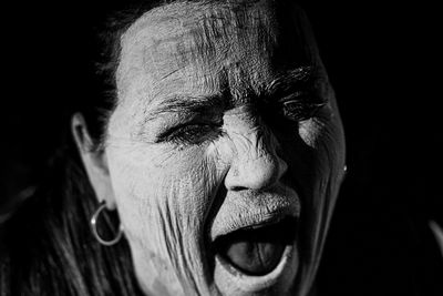 Close-up of woman screaming against black background