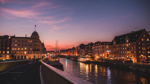 Illuminated buildings by river against sky at night