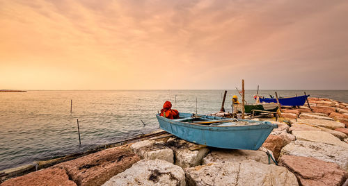 Fishing boat on shore against sky during sunset