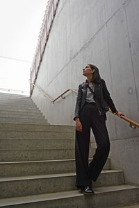 Low angle view of young woman standing on steps by wall