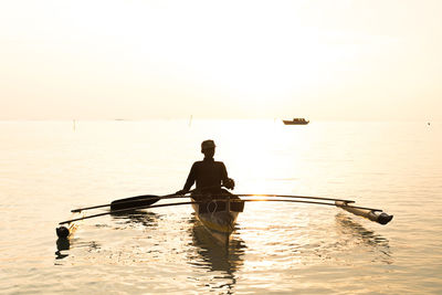 Man rowing boat in sea against sky