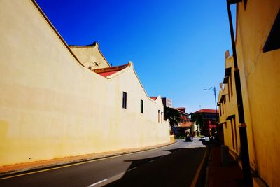 Road amidst buildings against clear blue sky