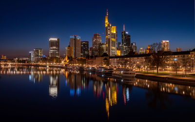 Illuminated buildings by river against sky at night